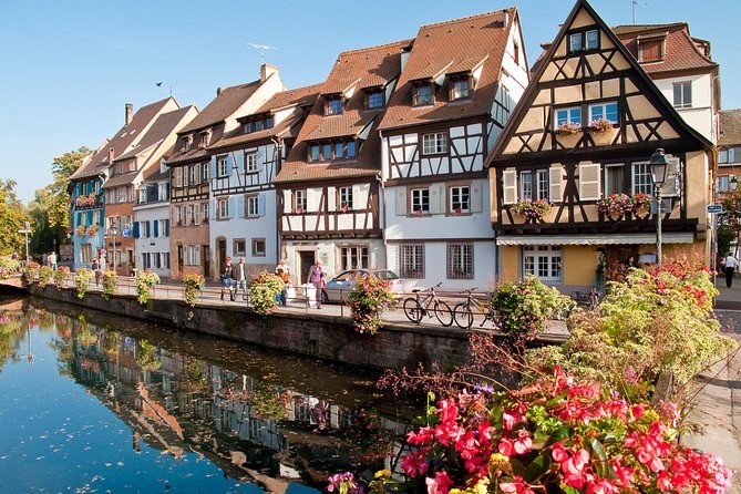 A row of half-timbered canal houses reflected in still water, geraniums on the bank