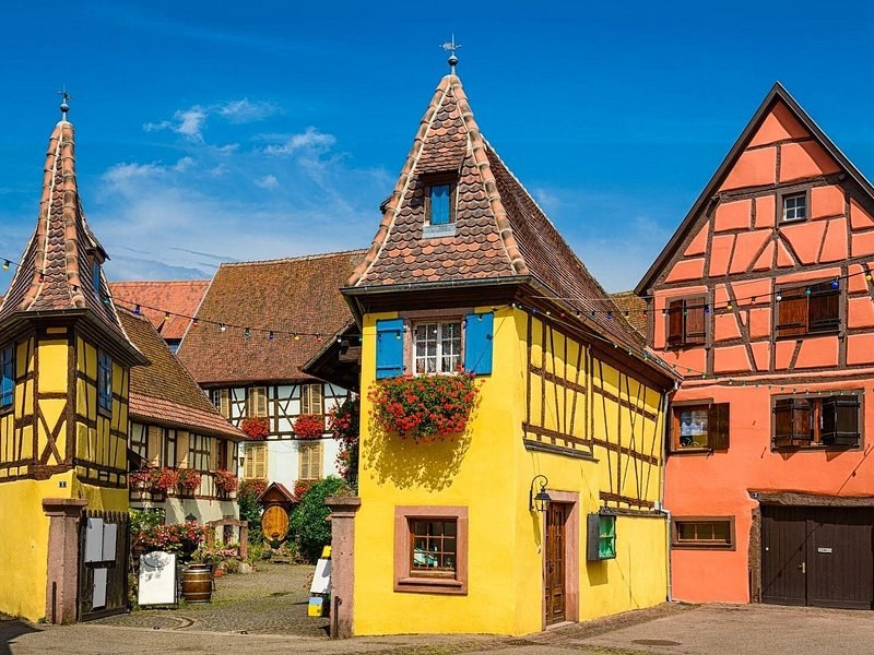 A pointed yellow half-timbered house on a village corner, an orange front beside it